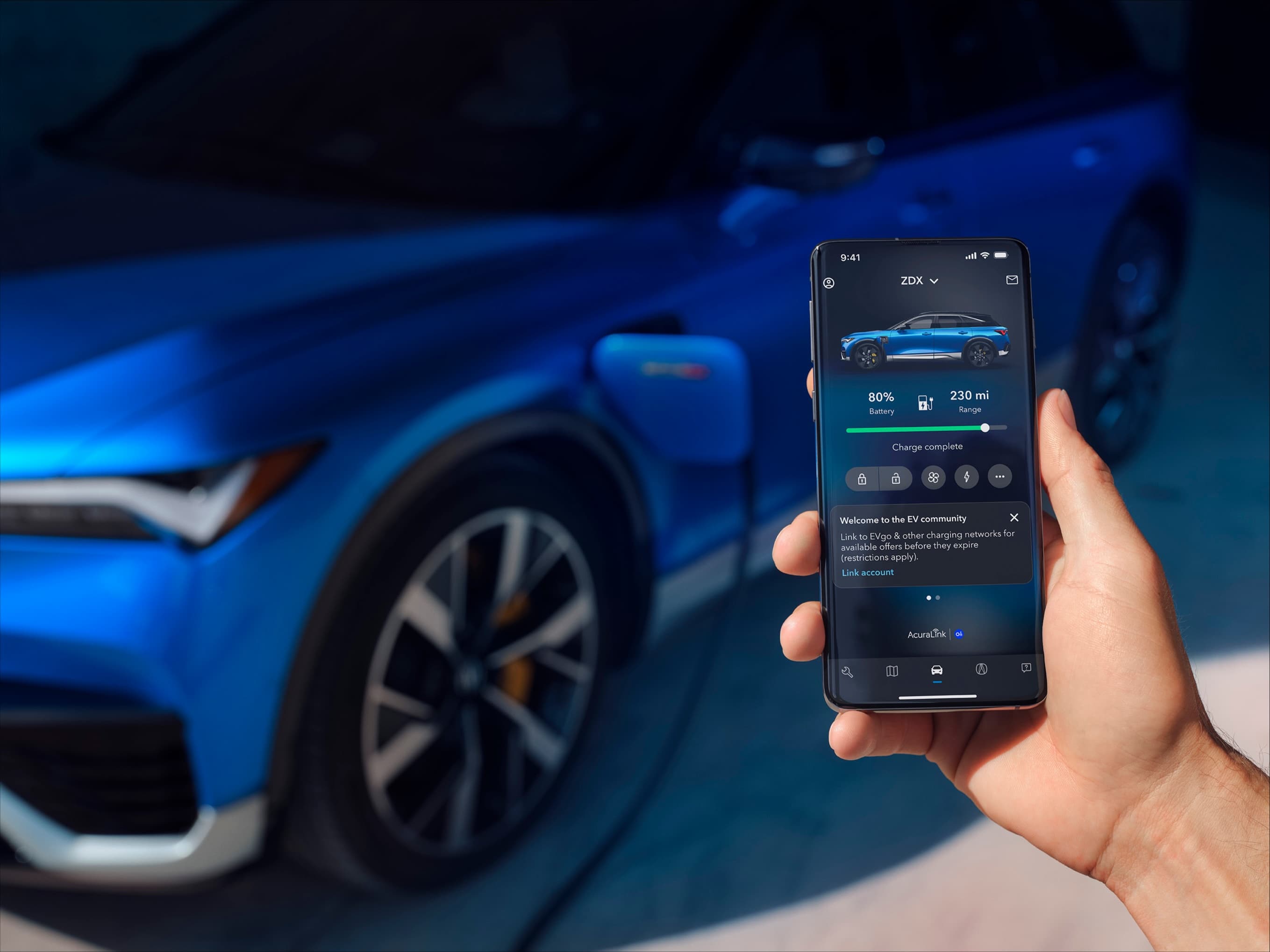 A hand holding the Acura EV app in front of a blue ZDX at a charger